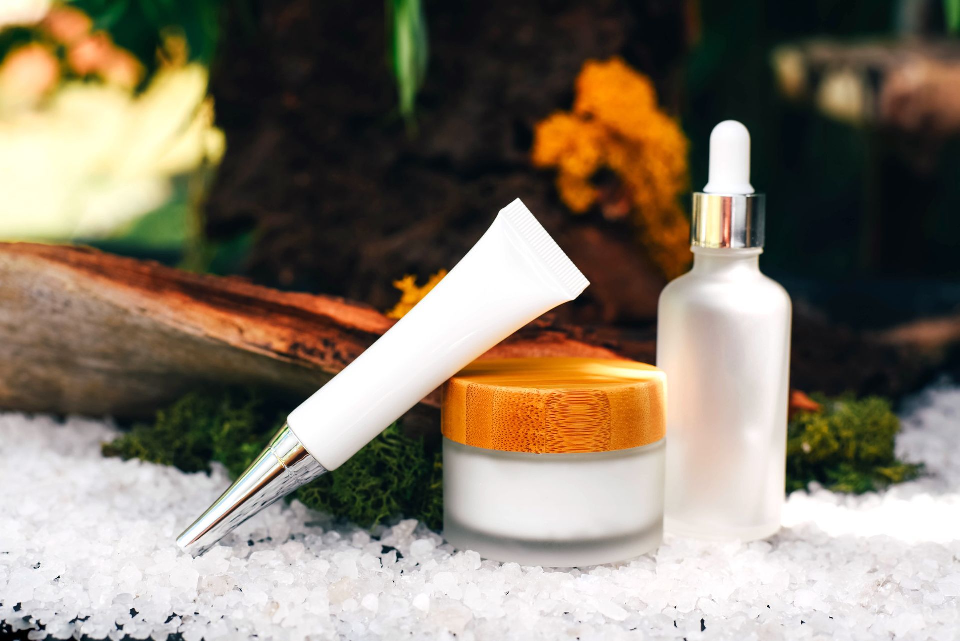 A bottle of lotion and a tube of cream are sitting on top of a pile of sea salt. A bottle of lotion and a tube of cream are sitting on top of a pile of sea salt.