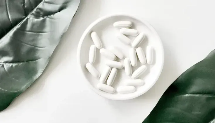 A bowl of pills is sitting on a table next to a green scarf.
