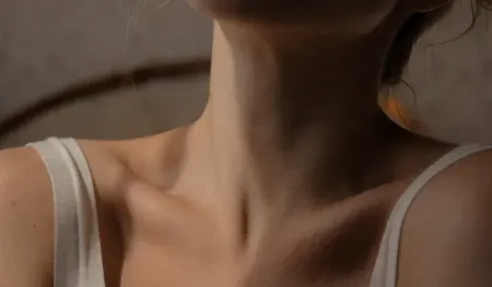 A close up of a woman 's neck and shoulder in a white tank top.
