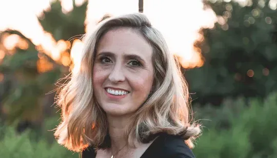 A woman with blonde hair is smiling for the camera in a field.