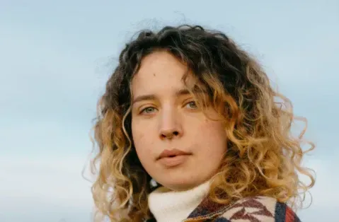 A close up of a woman with curly hair wearing a turtleneck sweater.