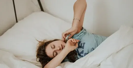 A woman is laying in bed talking on a cell phone.