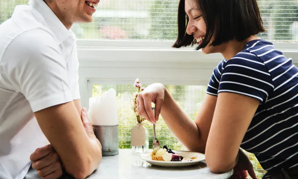 A man and a woman are sitting at a table eating dessert.