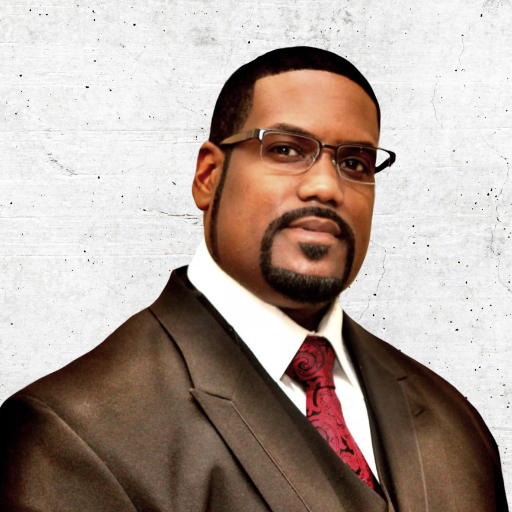 Portrait of a man in a brown suit and red tie, wearing glasses, against a light background