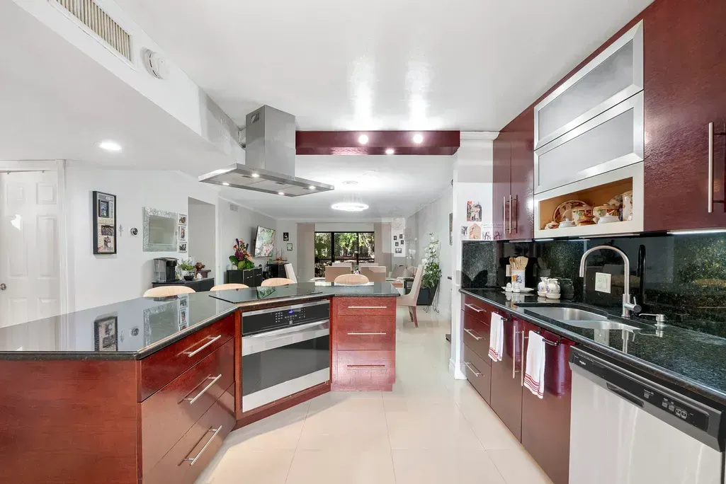 Modern kitchen with cherry cabinets, black countertops, stainless appliances, and a large island