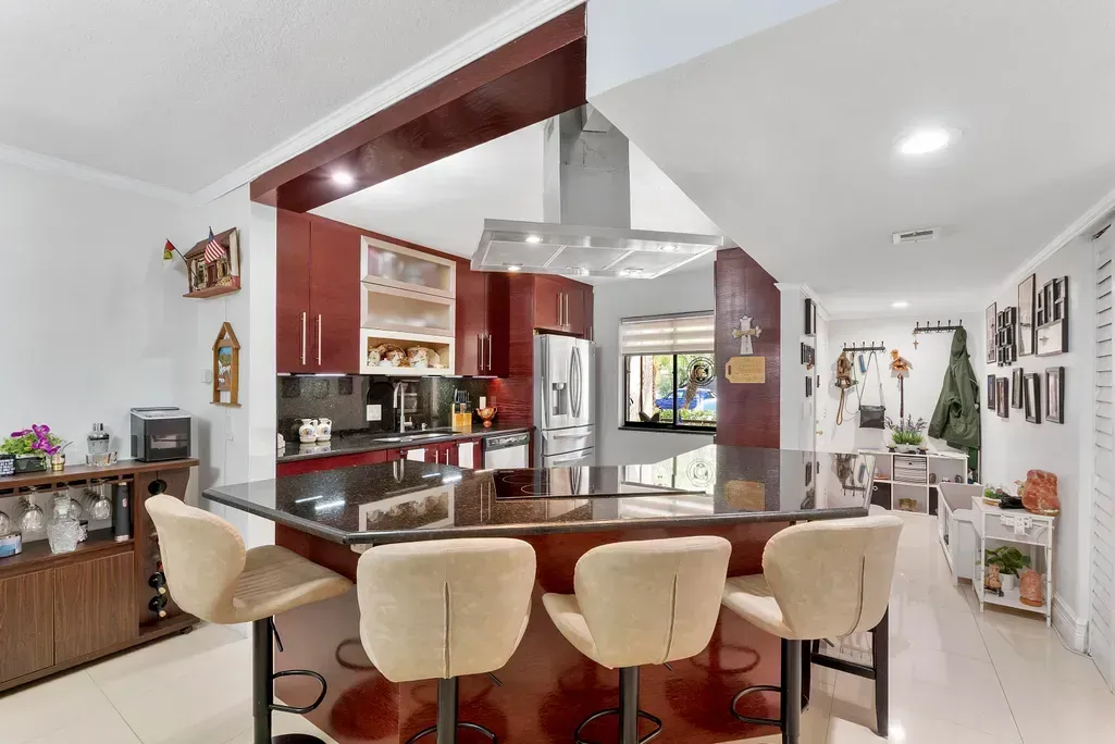 Modern kitchen with granite island, beige bar stools, and red wood accents
