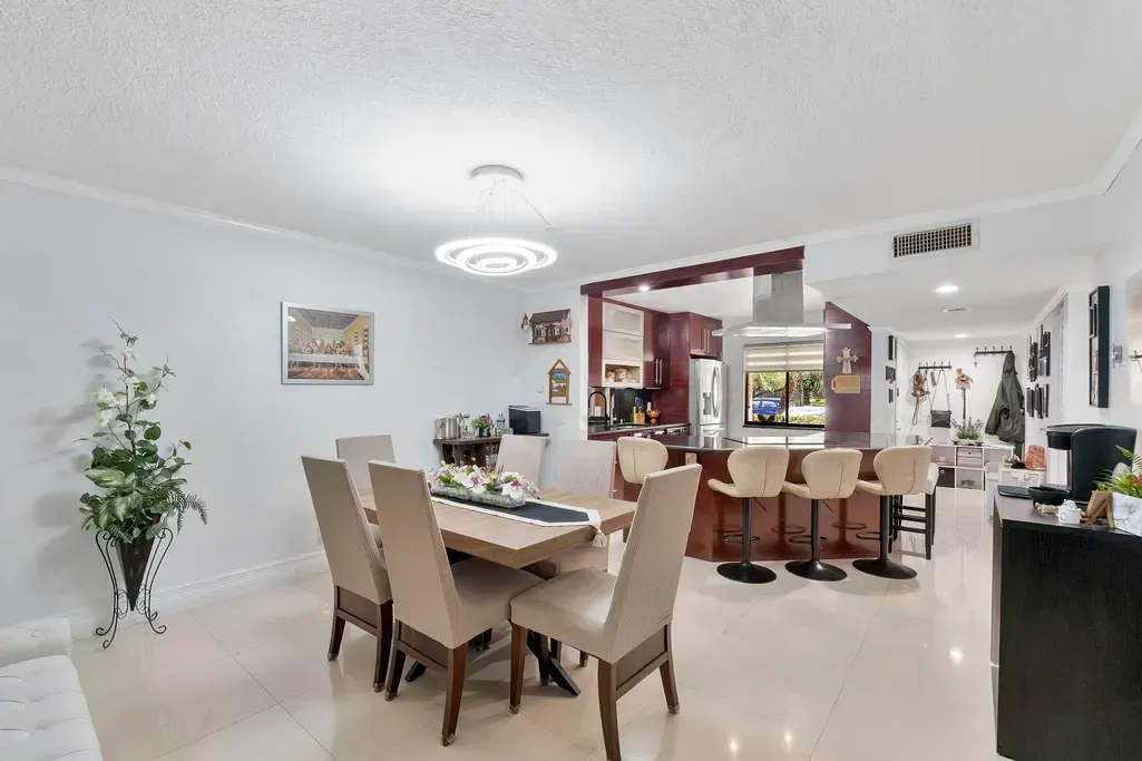 Bright open dining and living room with beige chairs, white walls, glossy floor, and a decorative chandelier