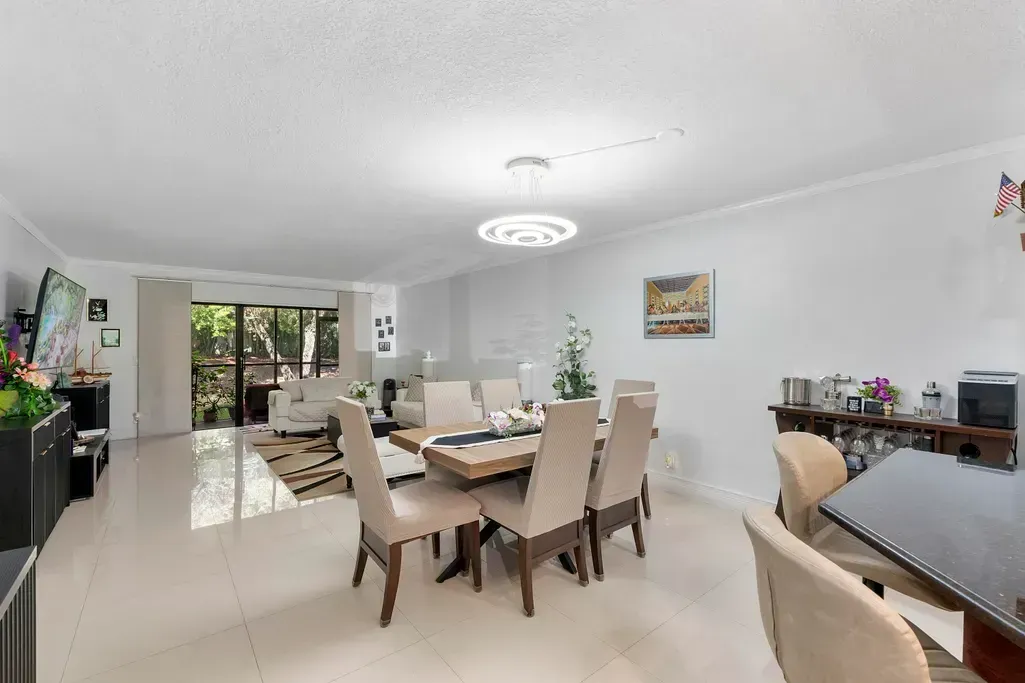 Bright dining room with beige chairs, table, and large windows opening to a patio.