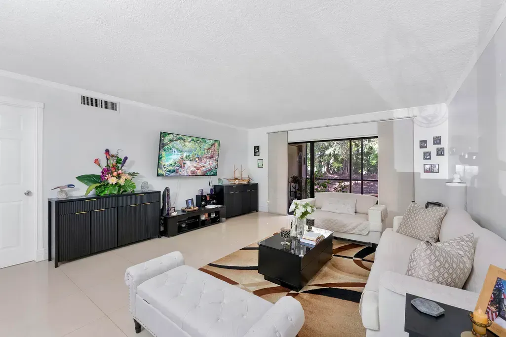 Bright living room with white sofas, coffee table, black sideboard, wall art, and large window view