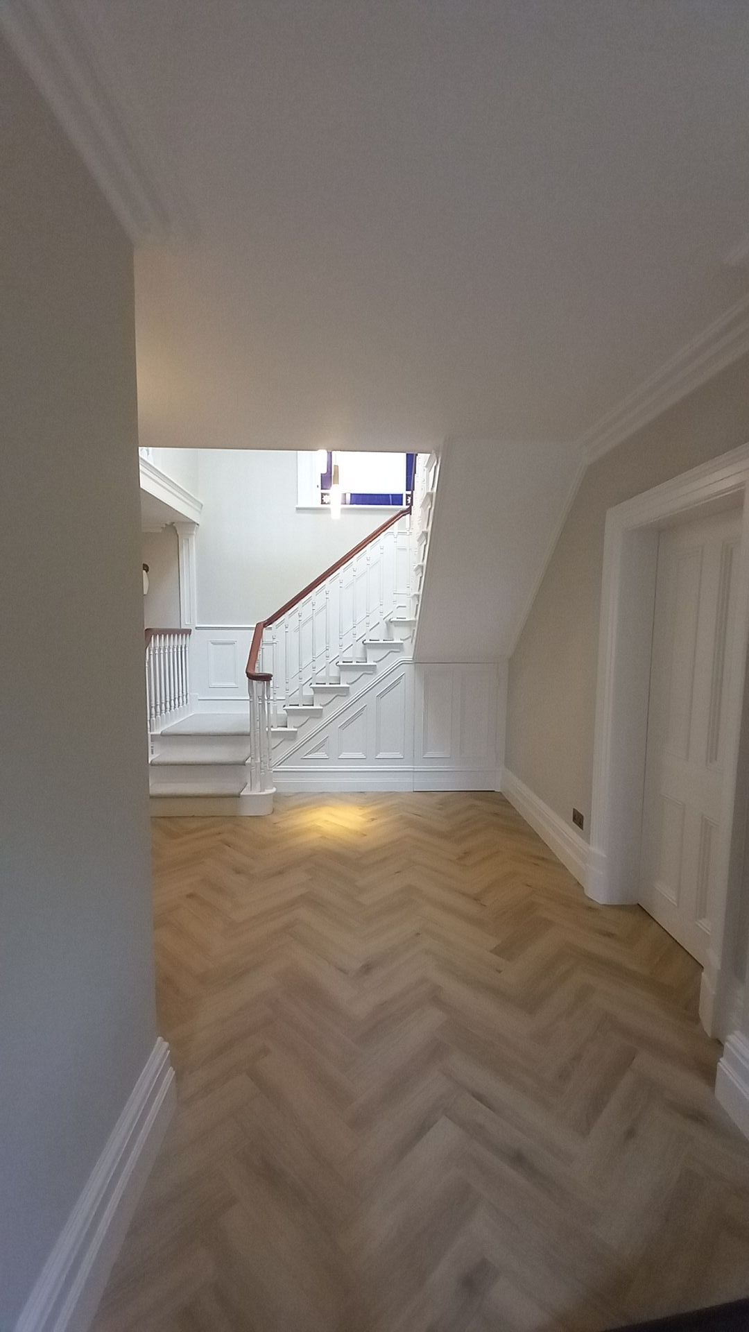 Flawlessly finished grand staircase – crisp white panelling and warm herringbone floor restored to timeless elegance