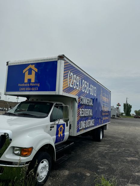 White moving truck with blue Hoss logo parked on gravel under overcast sky