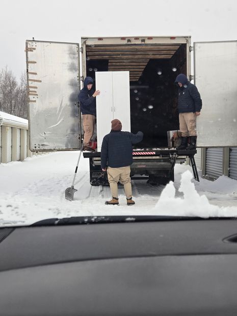 Workers loading a white appliance into a truck in a snowy parking lot
