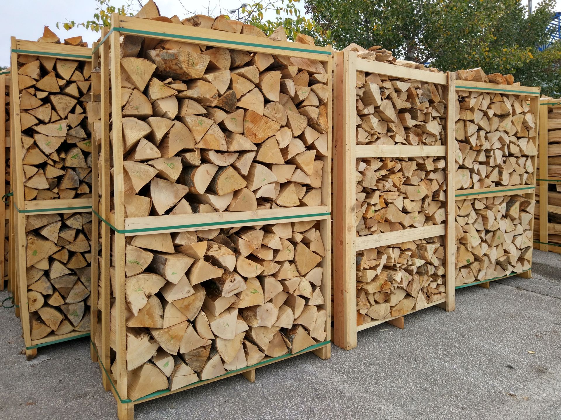 Stacked firewood in wooden racks outdoors beside a paved area.