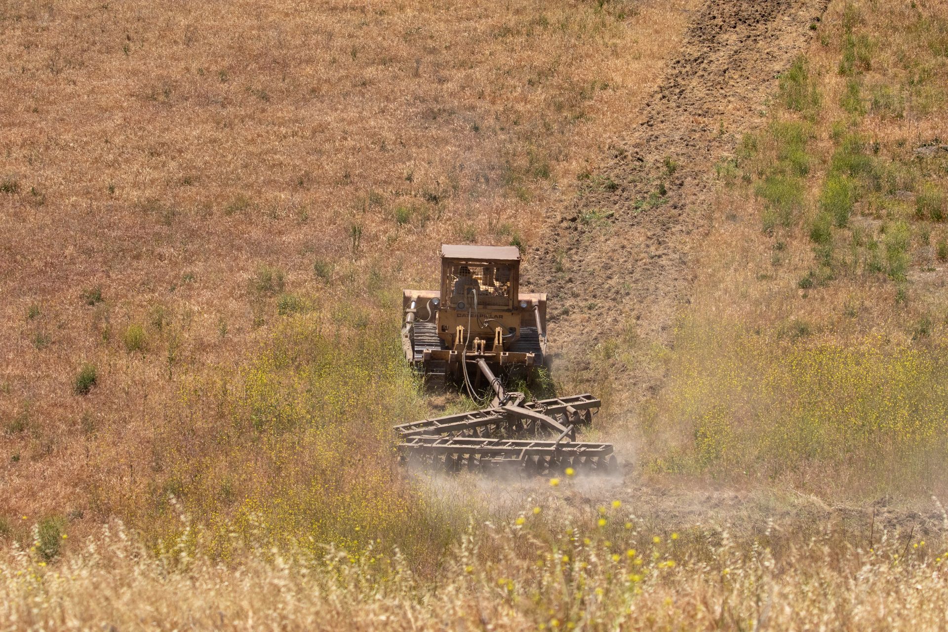 A tractor spraying dust over a dry, grassy field