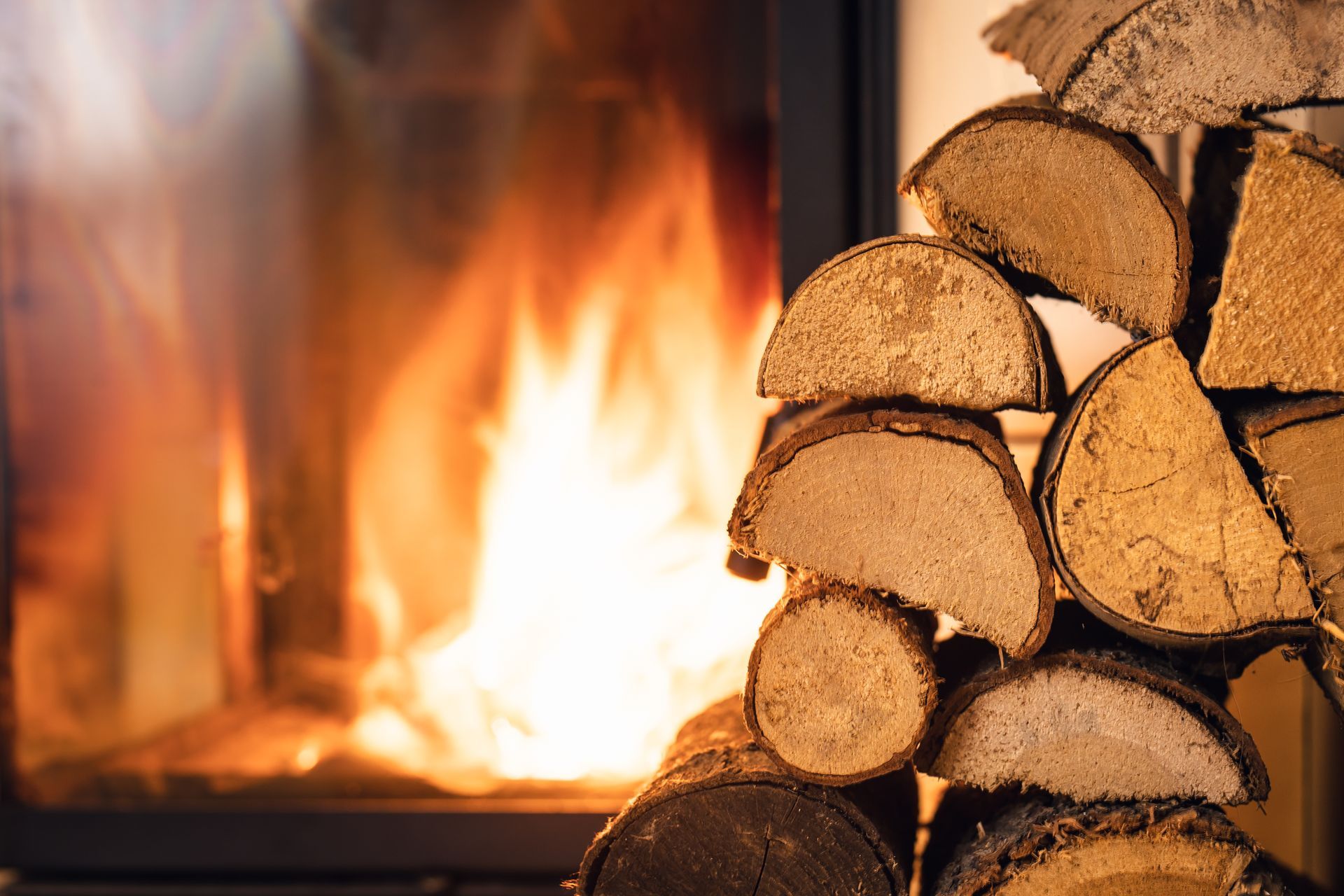 Fire burning in a fireplace beside stacked split firewood