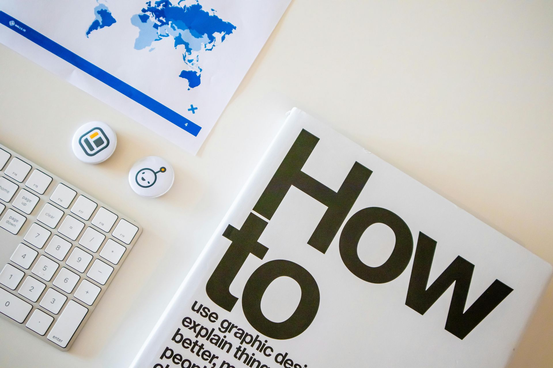 Desk with keyboard, blue world map print, small icons, and a “How to” booklet on a white surface