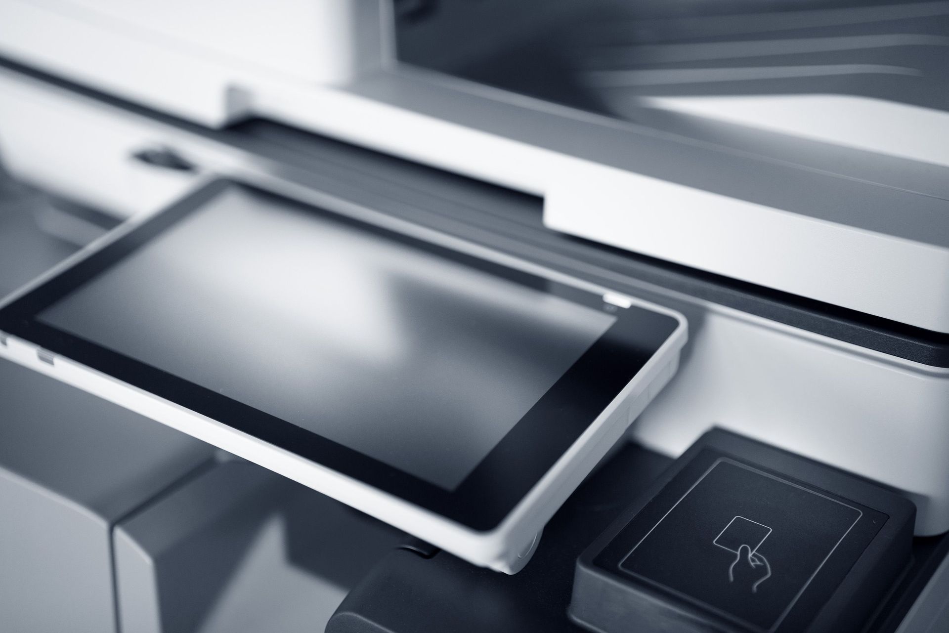 White touchscreen device on a sleek gray office machine, with a small control icon panel nearby