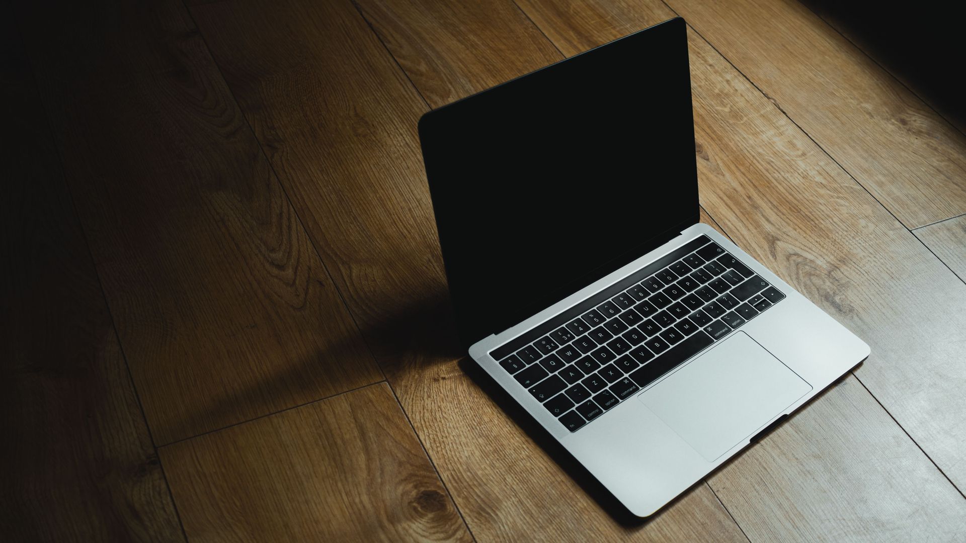 Open laptop on a wooden floor, screen dark in soft light.
