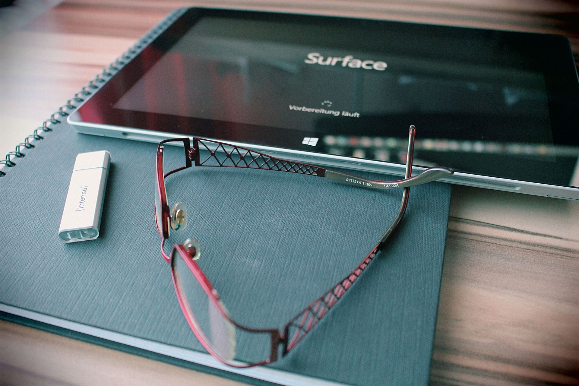 Surface tablet on a desk with eyeglasses and a small USB device nearby