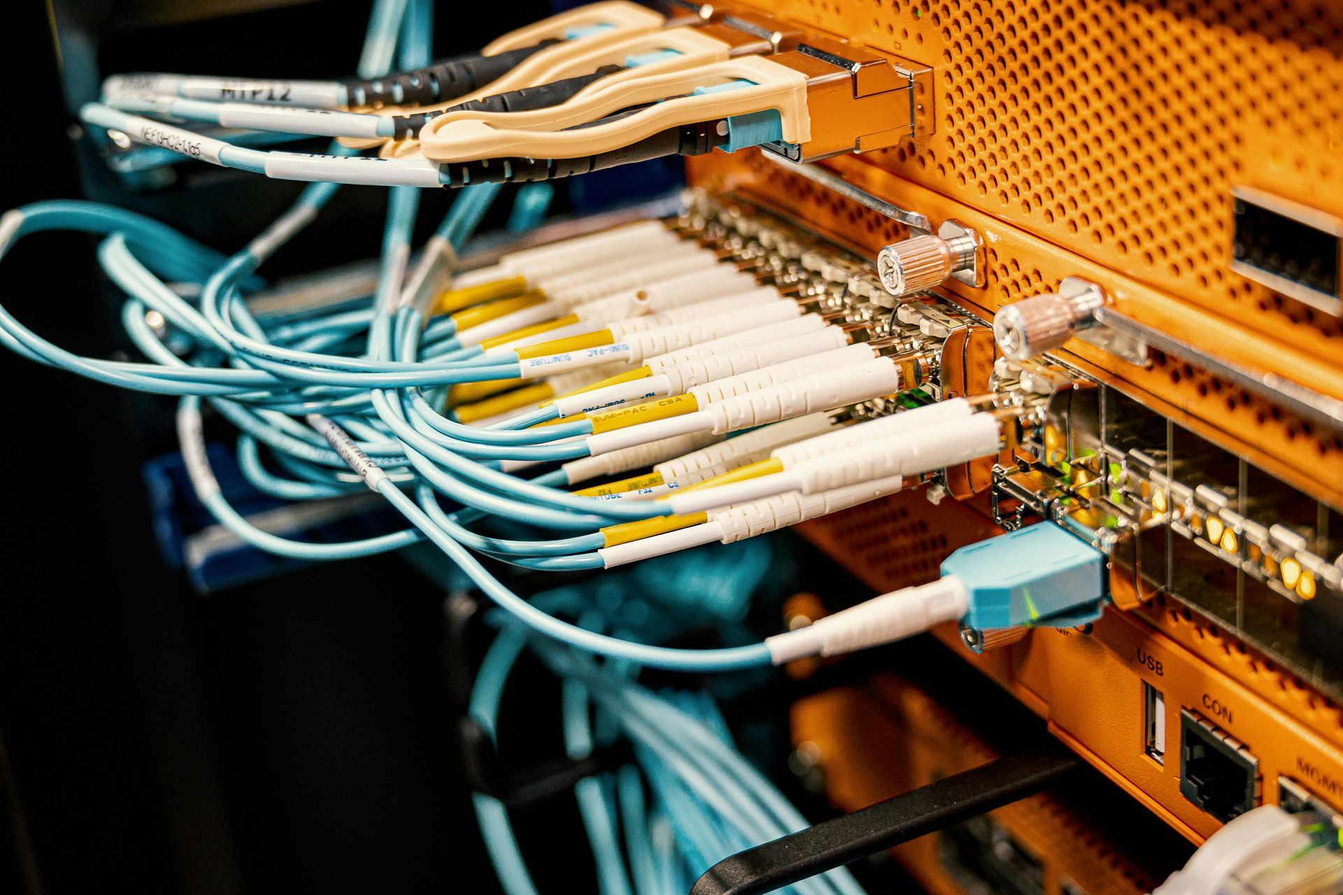 Network switch with many blue and white fiber optic cables plugged into an orange server rack