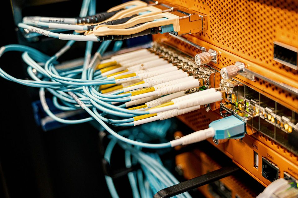 Network switch with many blue and white fiber optic cables plugged into an orange server rack