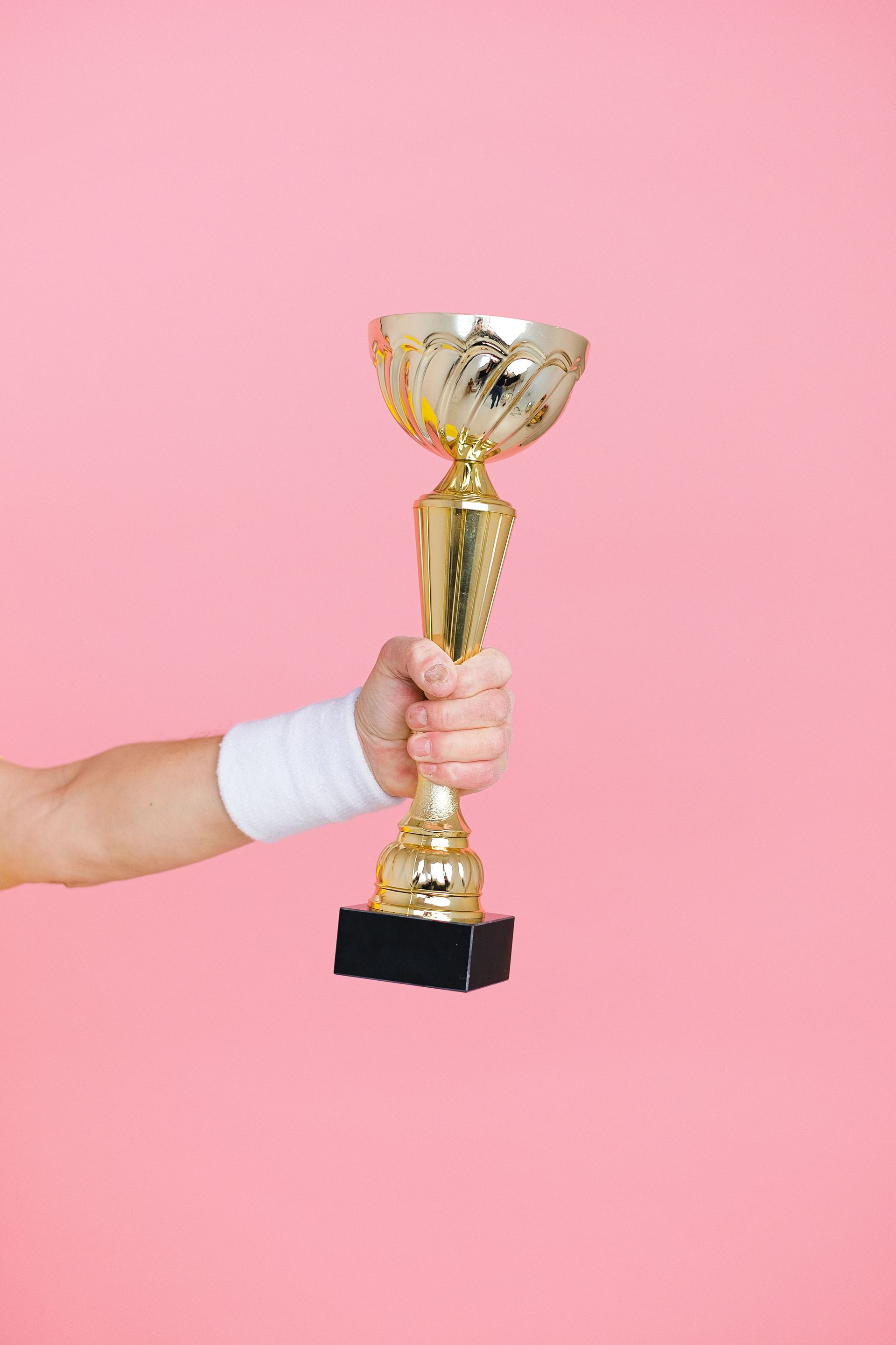 Hand holding a gold trophy against a pink background