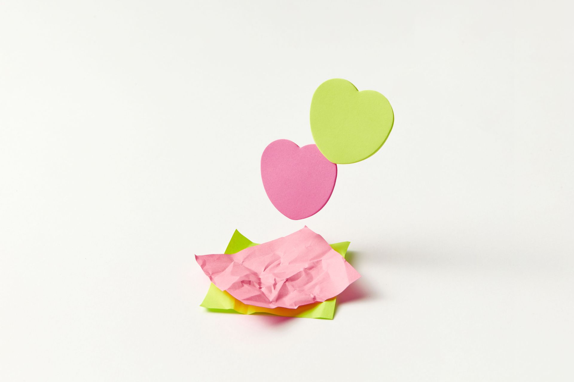 Pink and green paper hearts on a white background with a crumpled pink paper flower
