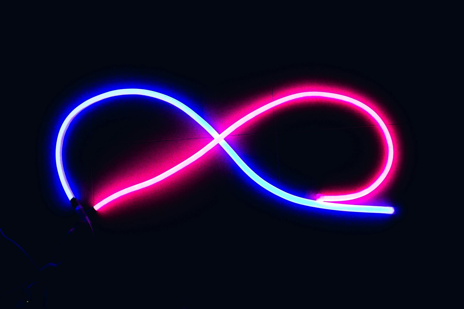Neon blue and pink light trail forming an infinity loop on a dark background