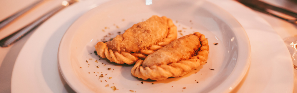 Dos pasteles dorados sobre un plato blanco con migas esparcidas.