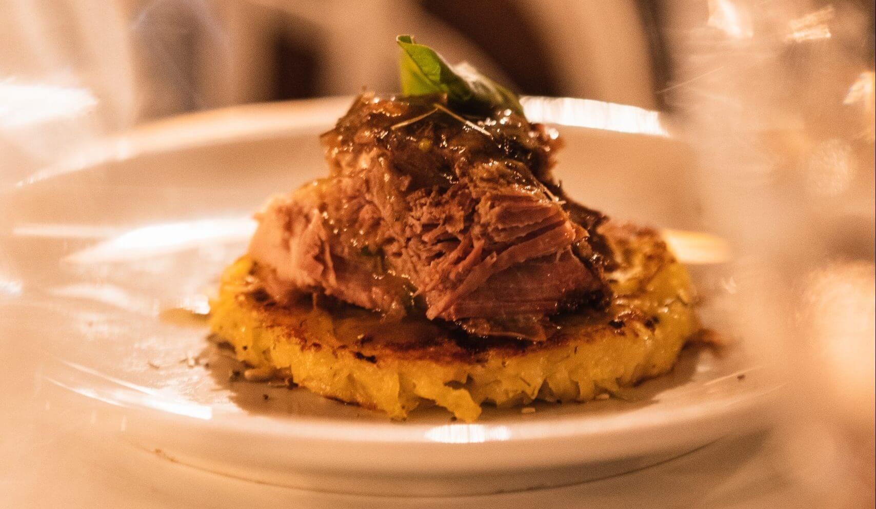 Plato gourmet con carne desmenuzada sobre una torta de maíz amarillo, adornado con hierbas.