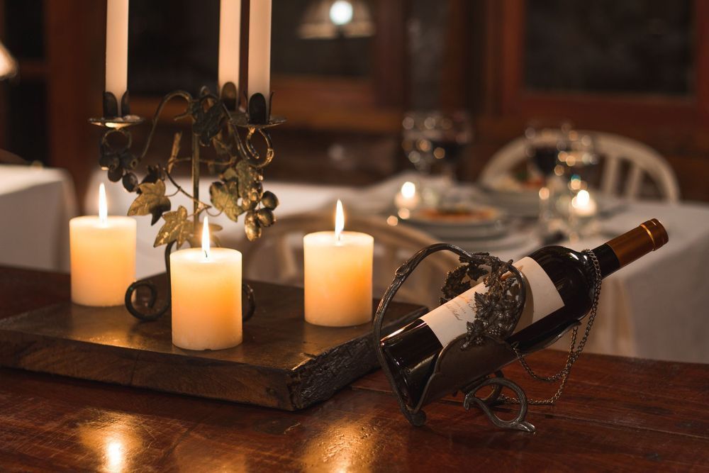 Velas y una botella de vino sobre una mesa de comedor con un centro de mesa decorativo, creando un ambiente cálido y romántico.