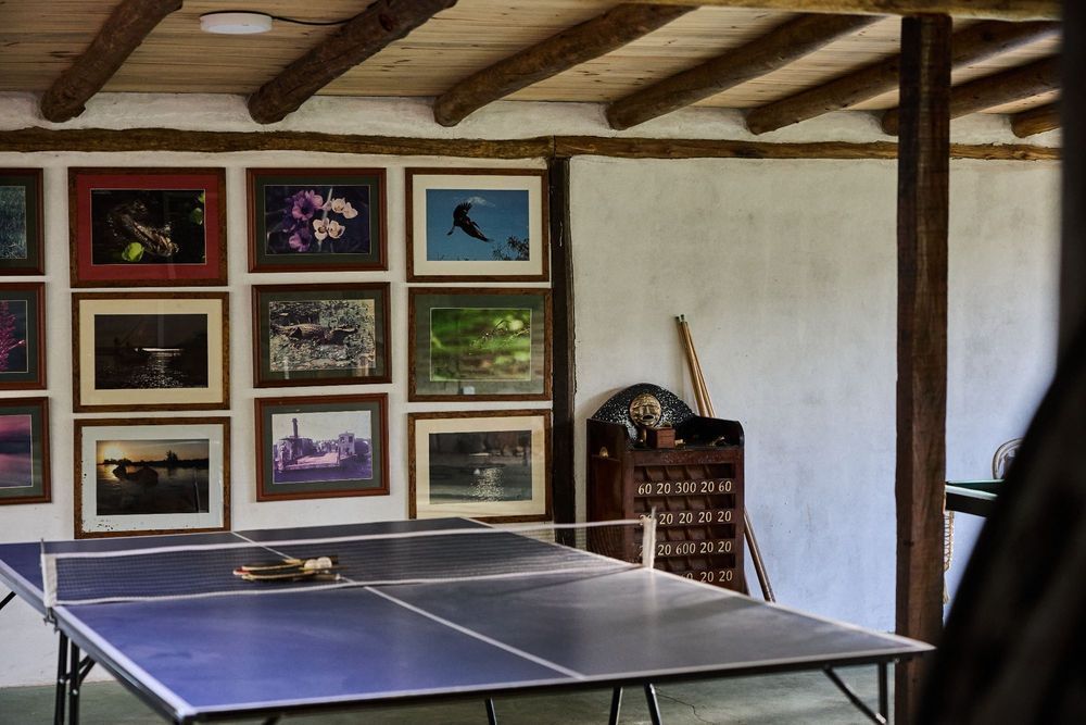 Mesa de ping-pong en una habitación rústica con fotos enmarcadas en la pared y un pequeño armario en la esquina.