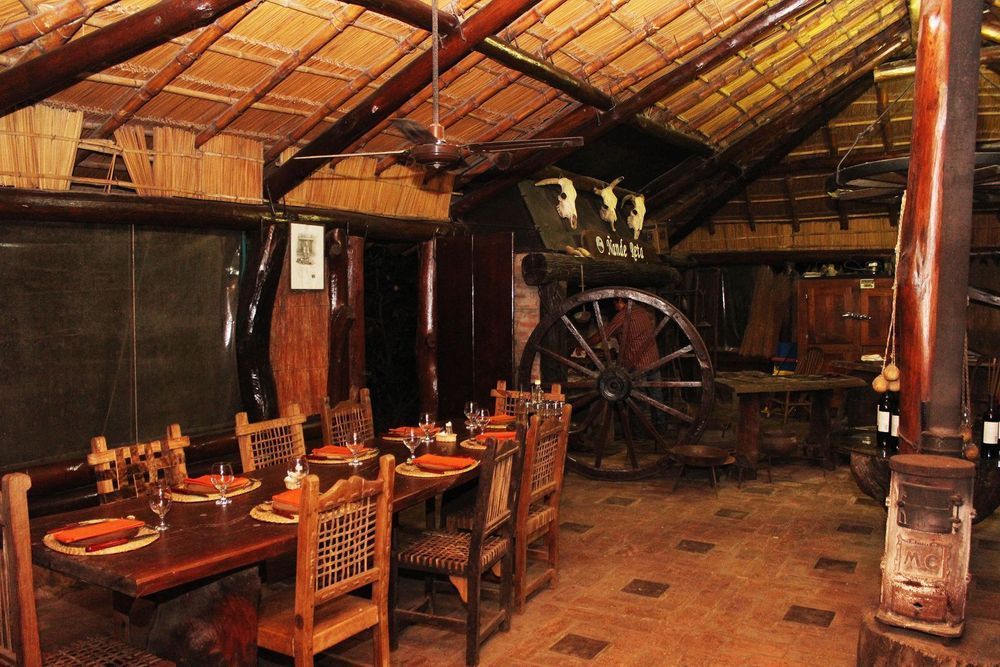 Comedor rústico de bambú con mesas y sillas de madera, y una gran rueda decorativa en la pared del fondo.