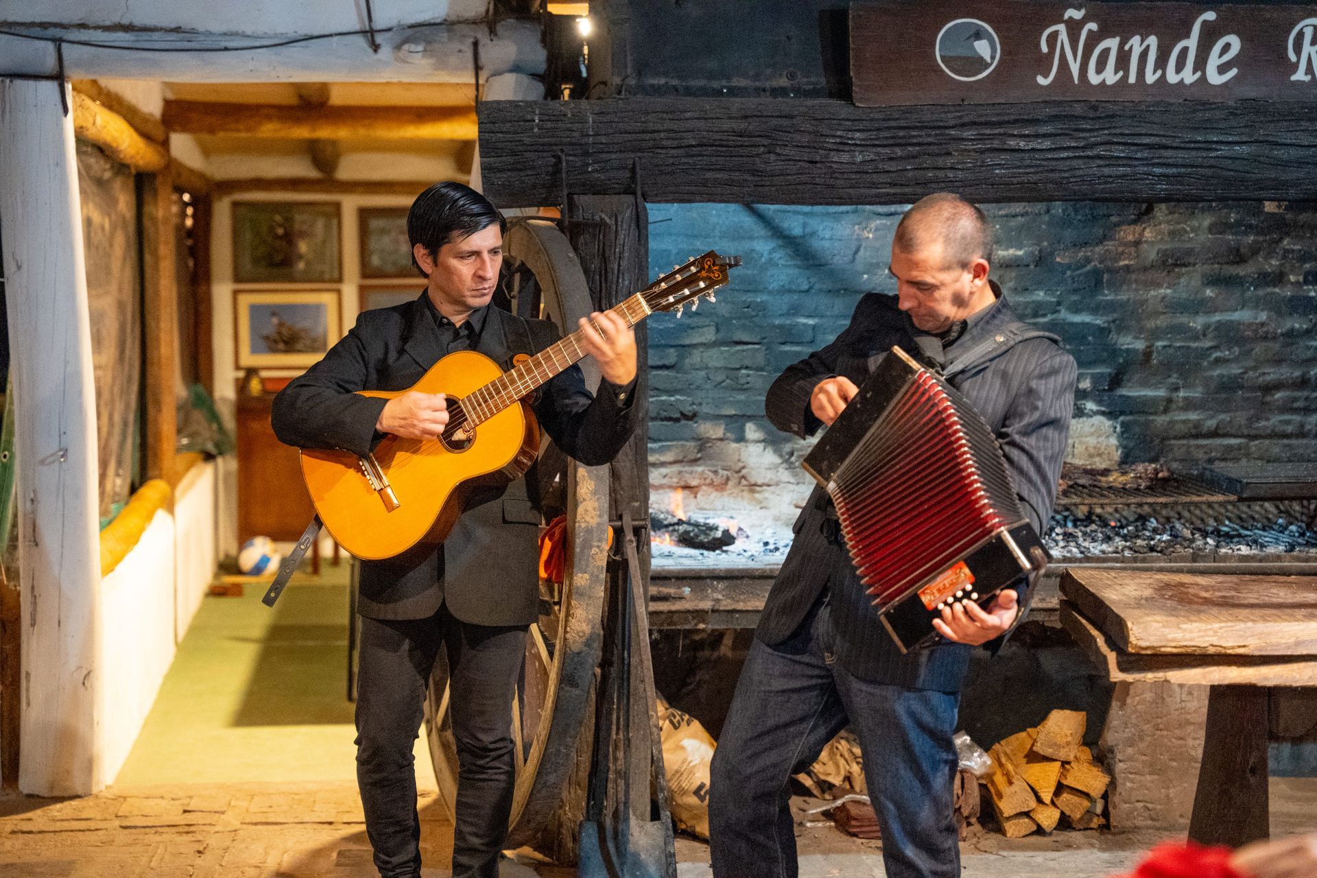 Dos músicos tocando la guitarra y el acordeón frente a una tienda rústica por la noche.