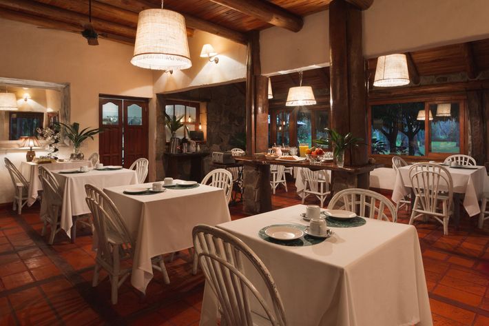 Acogedor comedor rústico con manteles blancos, vigas de madera e iluminación cálida.