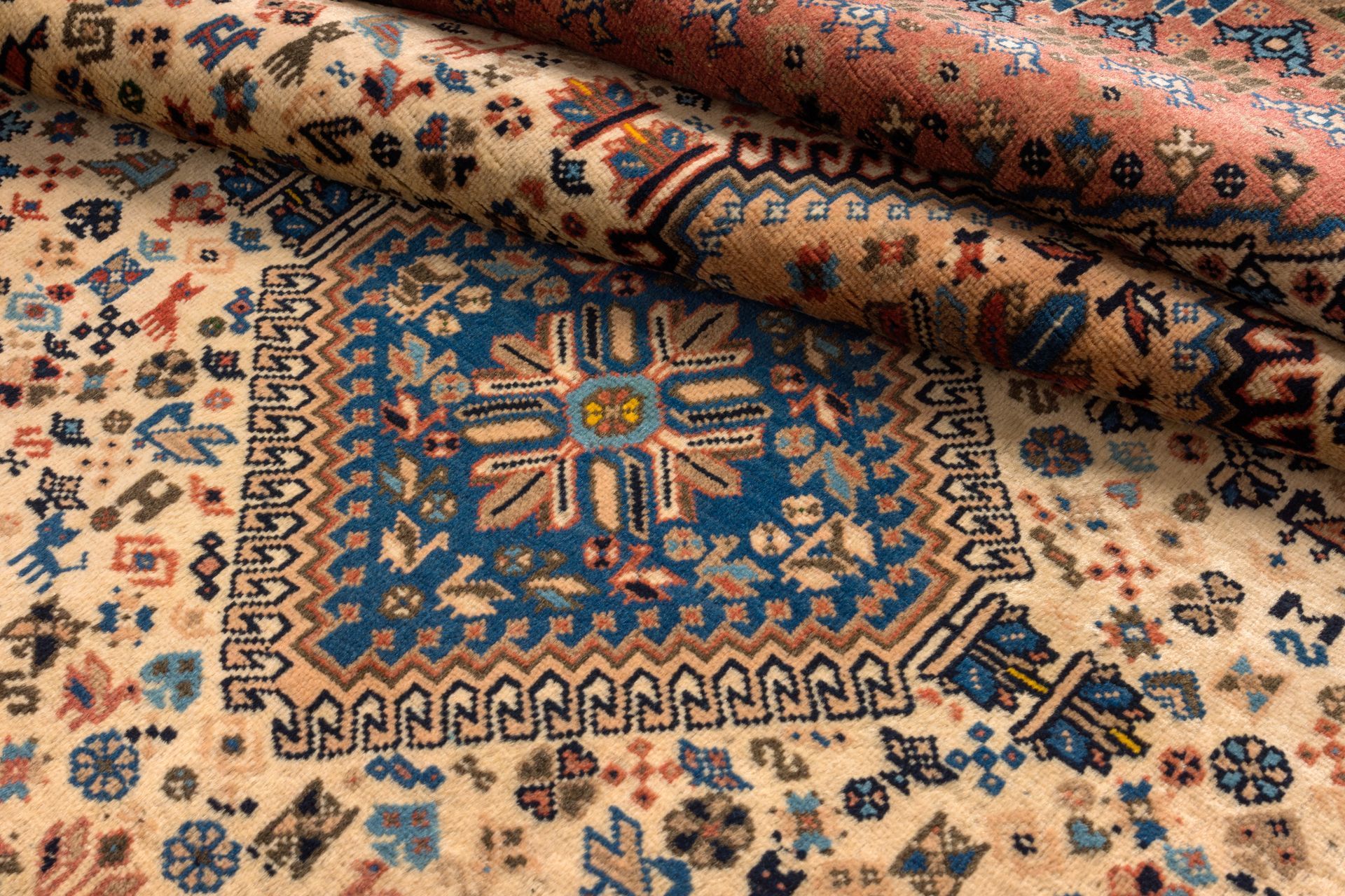 Rolled oriental-style area rug with intricate blue, red, and beige geometric patterns.