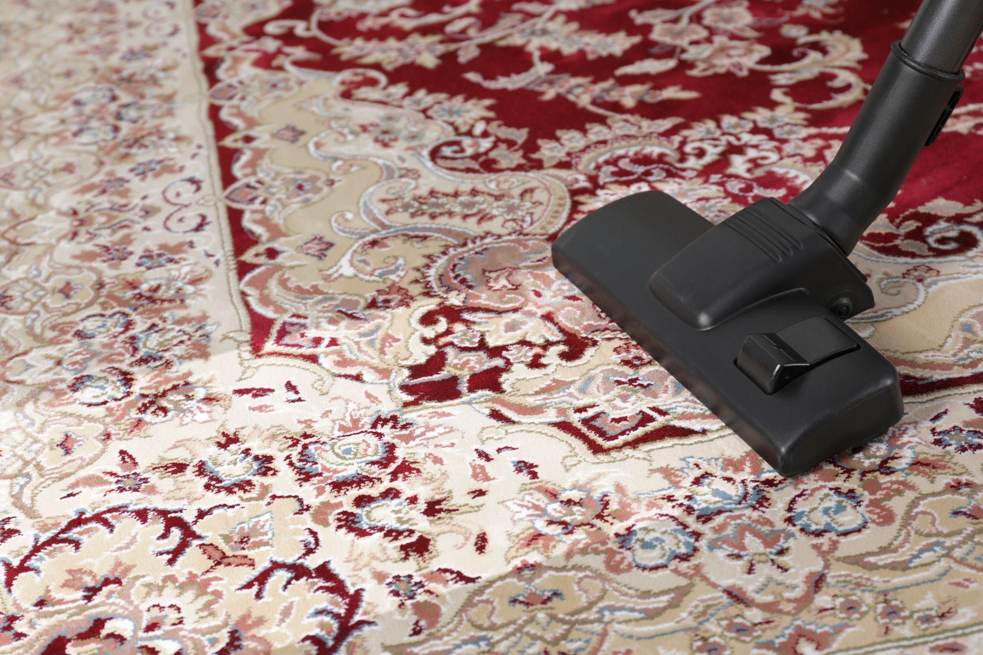 Vacuum cleaner head cleaning a patterned red and beige area rug during carpet maintenance. Vacuum cleaner head cleaning a patterned red and beige area rug during carpet maintenance.