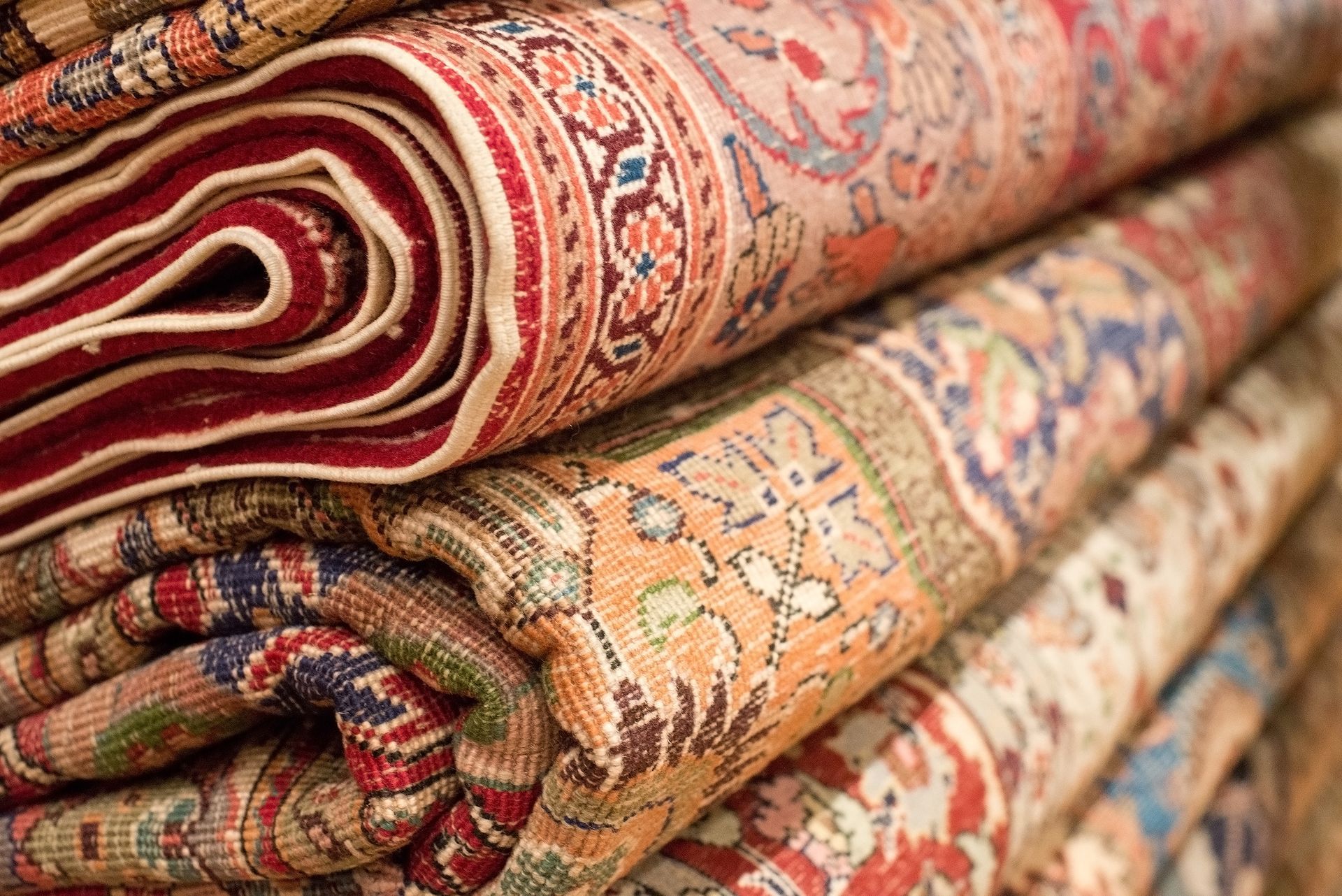 Rolled handmade oriental rugs stacked together, showcasing intricate patterns and fine weaving.