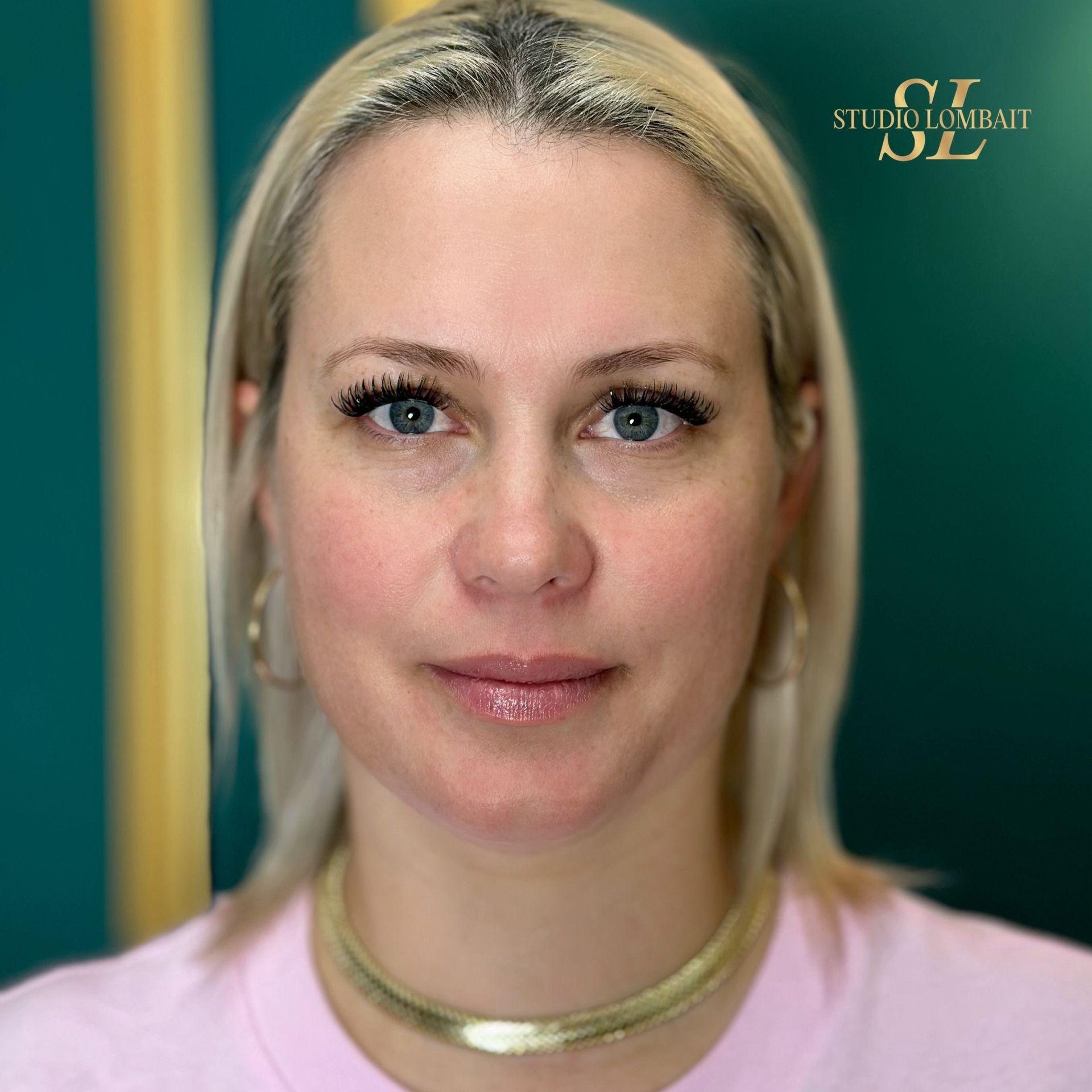 A woman wearing a pink shirt and a gold choker looks at the camera