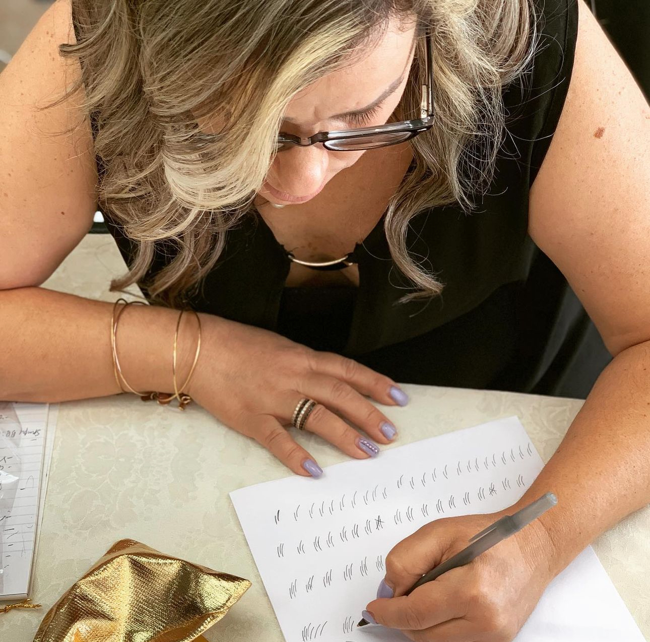 A woman wearing glasses is writing on a piece of paper