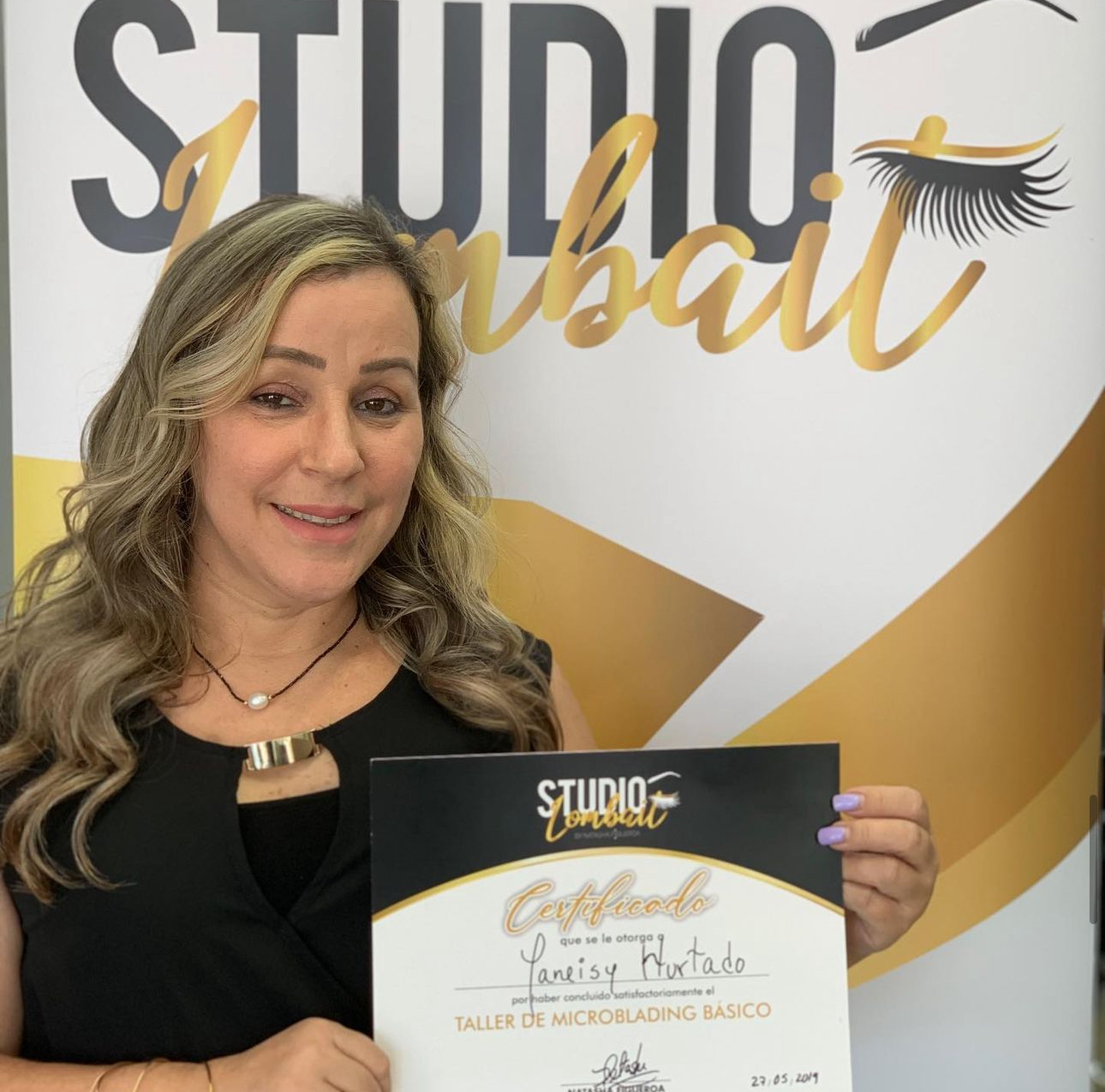 A woman is holding a certificate in front of a studio sign