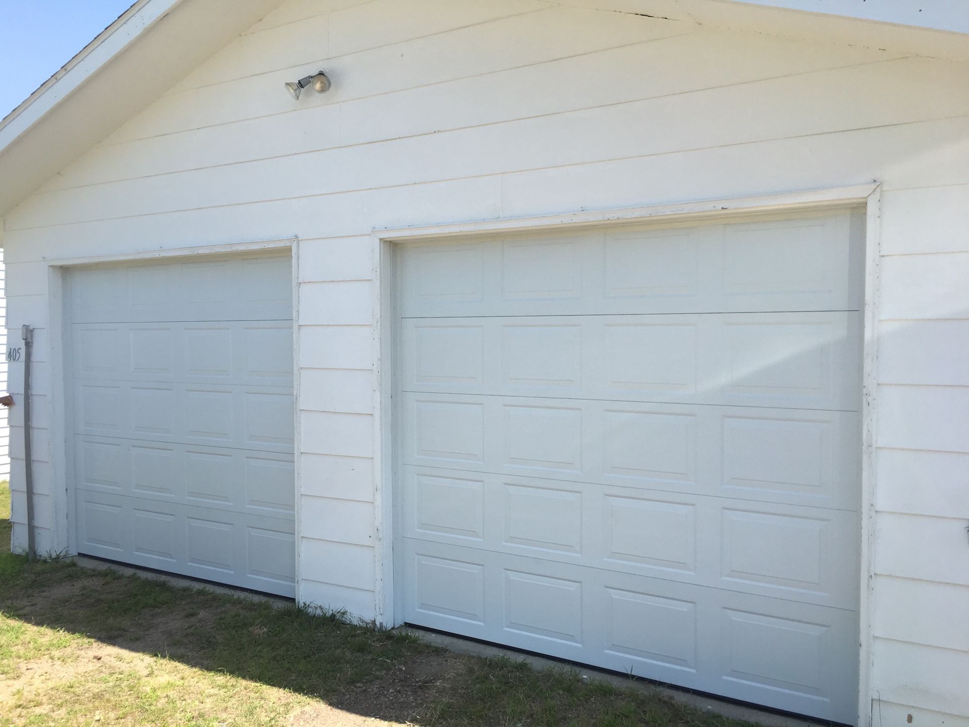 White two-car garage with closed doors, side by side, against a white-sided building with green grass in the foreground.