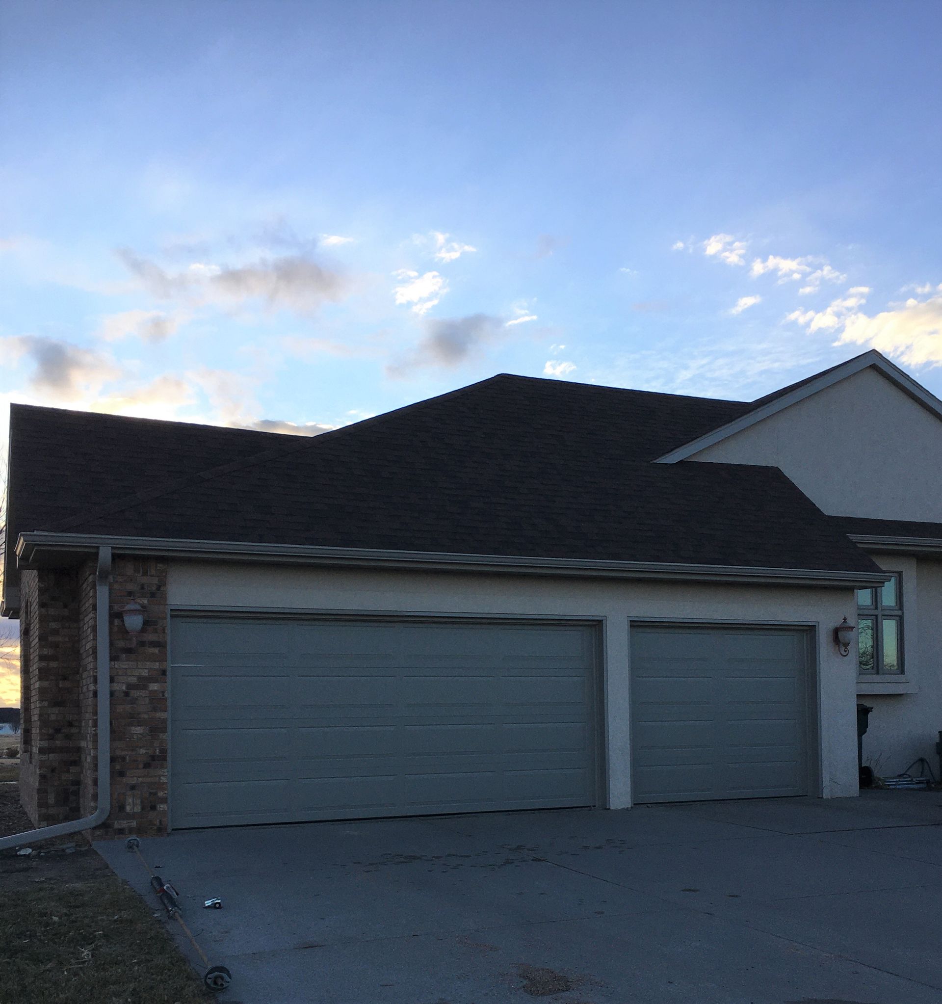 Two-car garage with gray doors, dark roof, beige stucco, and stone accents. Overcast sky.