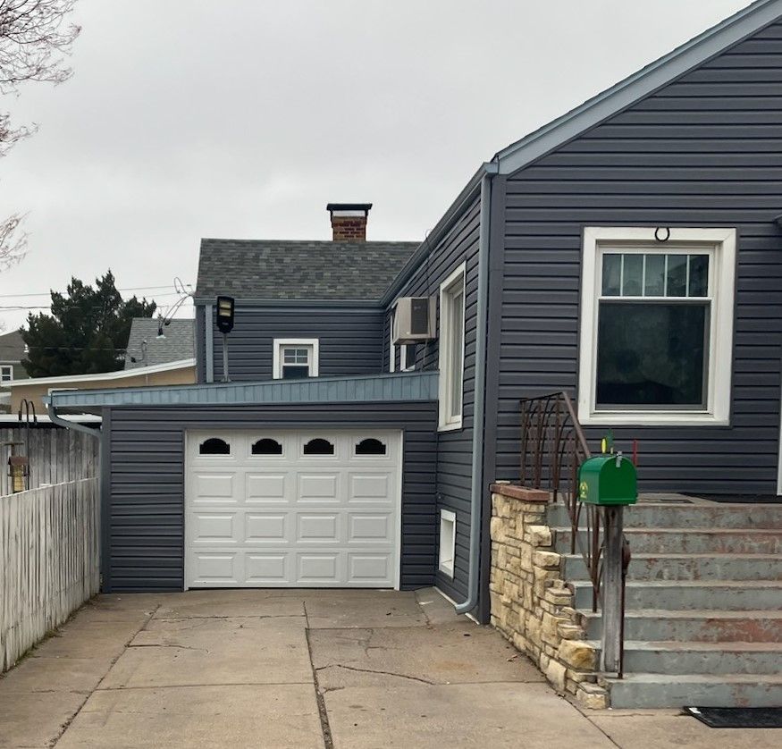 Gray house with a garage and white garage door. Concrete driveway and steps.