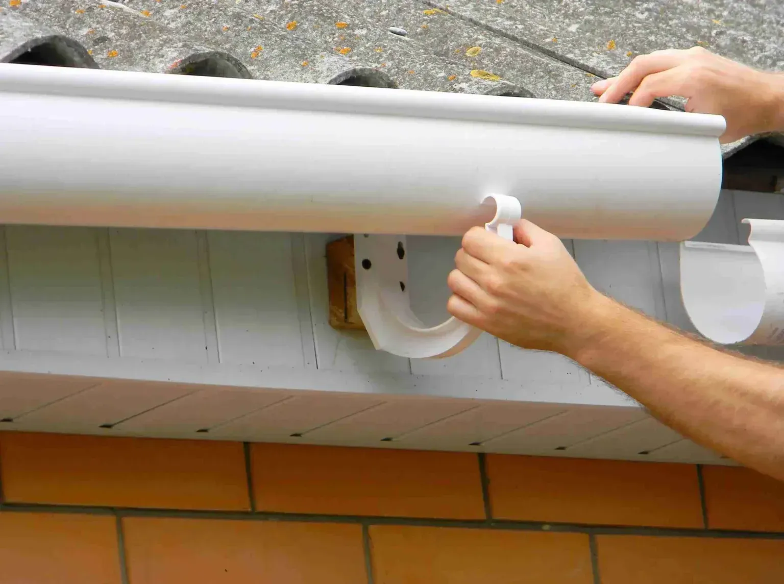 A person is installing a white gutter on a roof.