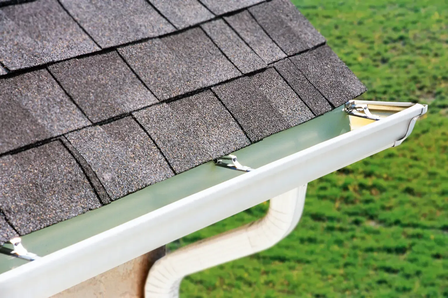 A close up of a gutter with a roof in the background.
