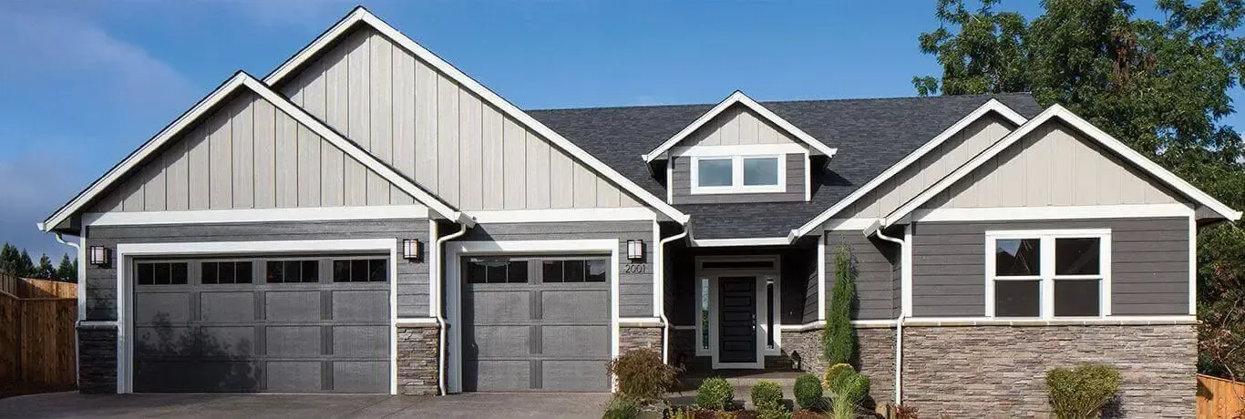 A large gray house with two garage doors and a blue sky in the background.