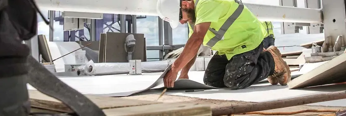 A construction worker is kneeling down on the ground at a construction site.