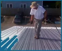A man is painting a metal roof with a sprayer.