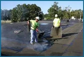 Two men are cleaning a parking lot with a broom.